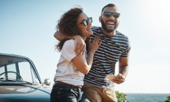 Happy couple leaning against their new vehicle they got with their vehicle loan at the beach