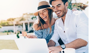 Man and woman on the beach smiling looking at the computer and holding their LimeRewards Visa Signature Credit Card